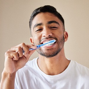 Man in white shirt smiling while brushing teeth