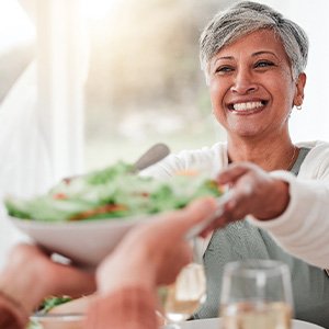 Smiling woman grabbing salad bowl across the table