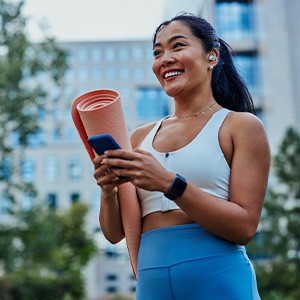 Smiling woman walking on park with workout mat