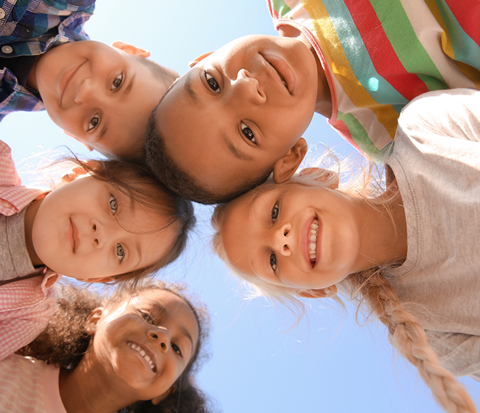 Five kids in a circle putting their heads together in the middle and looking down at the camera