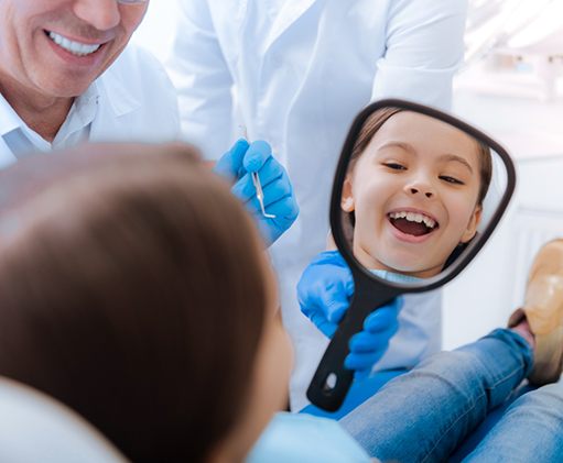 Child in the dental chair looking at their teeth in a mirror