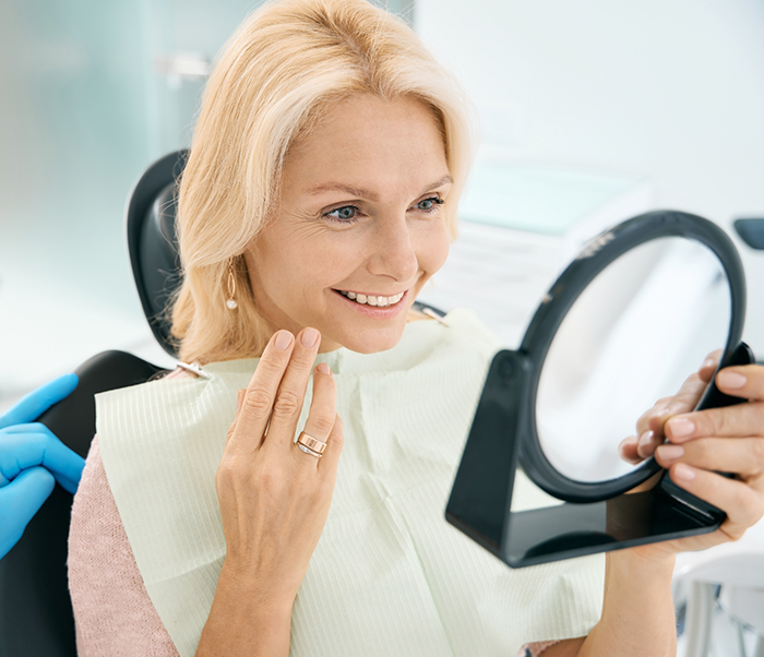 Woman in the dental chair looking in the mirror at her new smile after cosmetic dentistry in Justin