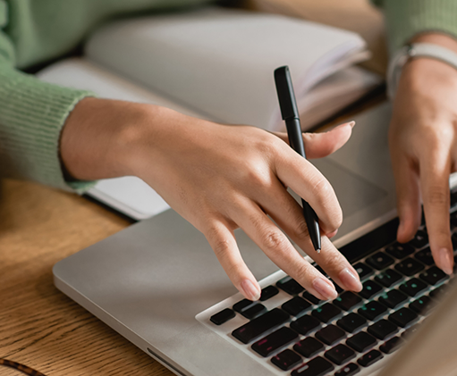 Perosn holding a pen and typing on a laptop