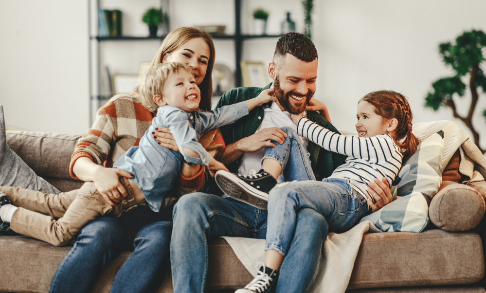Family of four laughing on their couch together after seeing their dentist in Justin