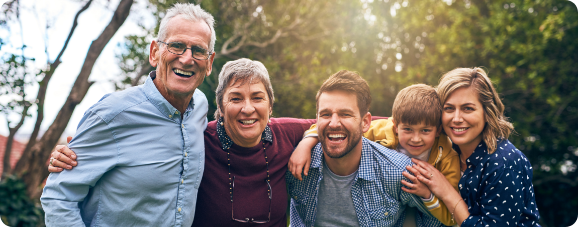 Three generations of a family smiling outdoors with green trees in the background
