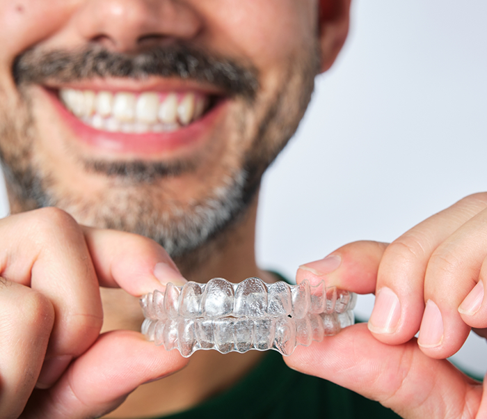 Smiling man holding two Invisalign clear aligners in Justin
