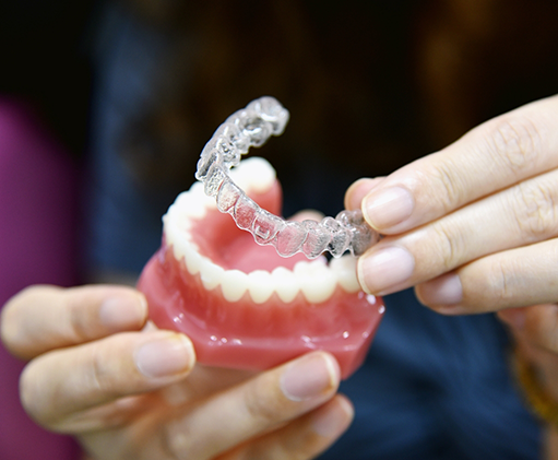 Dentist placing an Invisalign clear aligner over a model of an arch of teeth