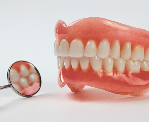 Set of full dentures next to a dental mirror