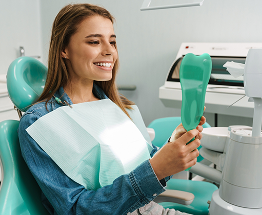 Woman in the dental chair looking at her smile in a mirror