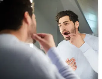 Man looking closely at one of his teeth in a mirror
