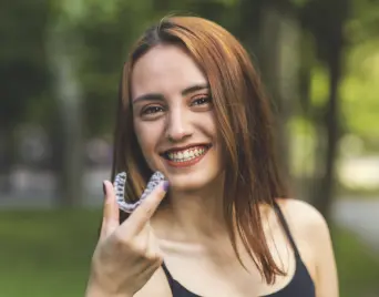 Smiling woman holding a clear aligner outdoors