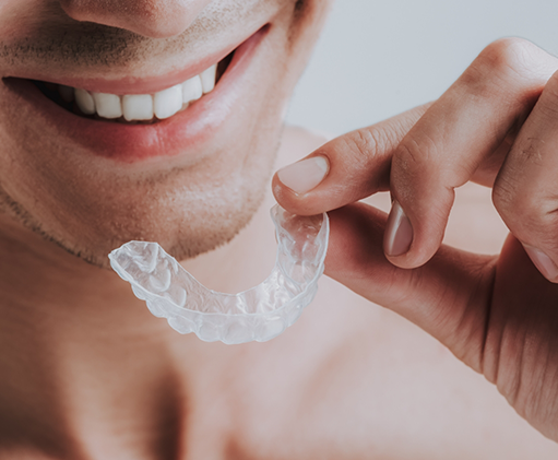 Smiling person holding a clear nightguard close to their mouth