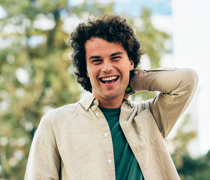 Man with curly brown hair smiling in the sun after root canal treatment in Justin