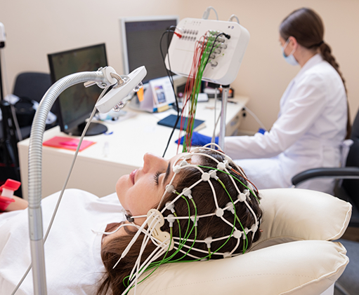 Sleeping woman with electrodes attached to her head while a scientist observes her readings on a computer