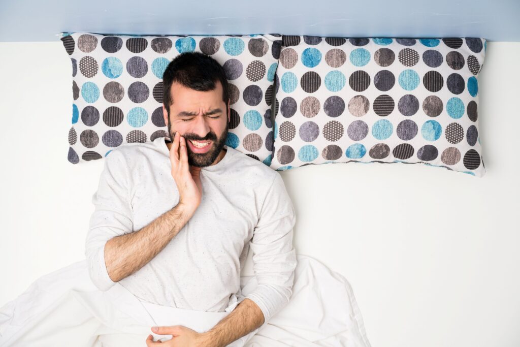 Bird's eye view of man laying on polka dot pillow touching jaw in pain